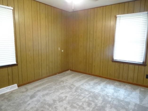 empty room featuring a ceiling fan, visible vents, baseboards, wood walls, and carpet flooring