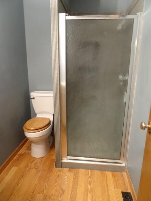 bathroom featuring a shower stall, toilet, wood finished floors, and visible vents