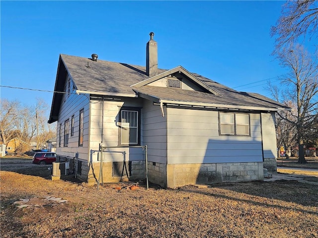 rear view of property with a shingled roof, a chimney, and cooling unit