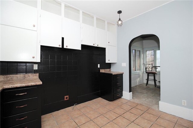 kitchen with light tile patterned flooring, light countertops, arched walkways, white cabinetry, and backsplash