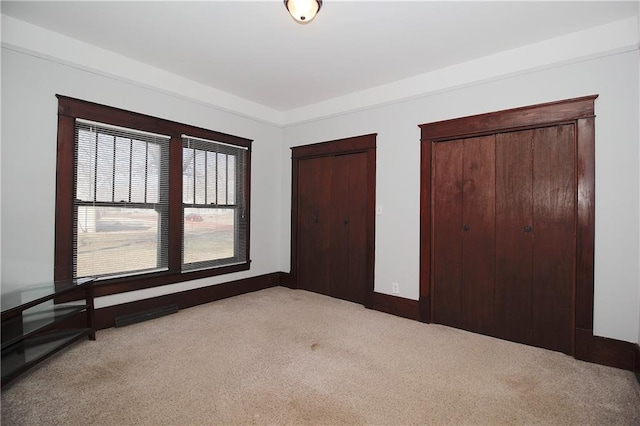 unfurnished bedroom with carpet floors, baseboards, and multiple closets