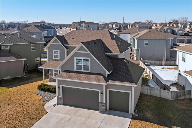 view of front of home featuring a shingled roof, fence, a residential view, stone siding, and driveway