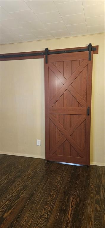unfurnished room with a barn door, dark wood-type flooring, and baseboards