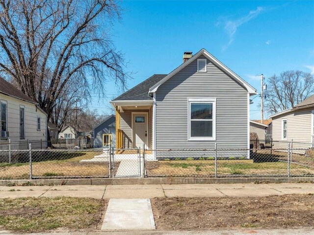 view of front of property featuring a fenced front yard, a shingled roof, a chimney, and a gate