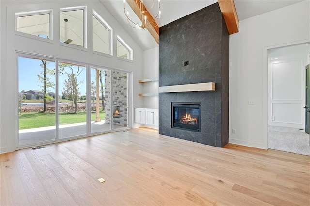 24936 W 98th Pl, Lenexa, KS 66227 - unfurnished living room with a tiled fireplace, wood finished floors, a towering ceiling, built in shelves, and a chandelier