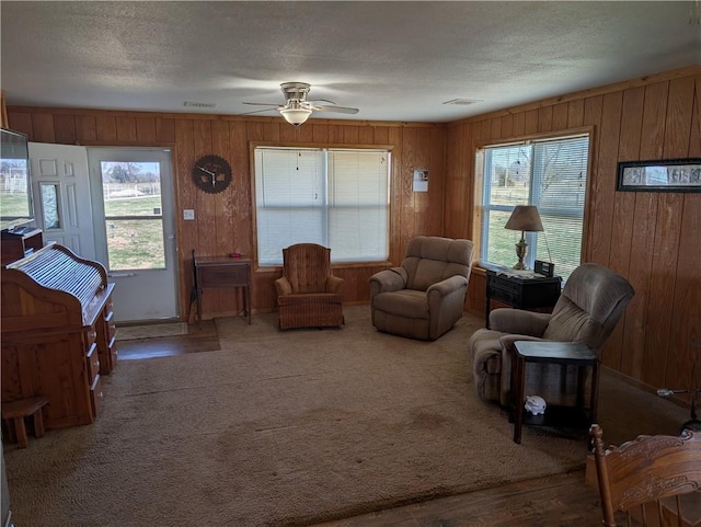 carpeted living area featuring visible vents, wood walls, a textured ceiling, and a ceiling fan