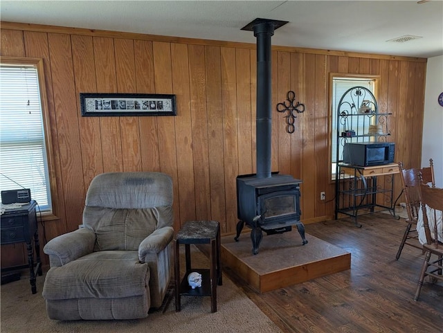 sitting room with visible vents, a wood stove, wooden walls, and wood finished floors