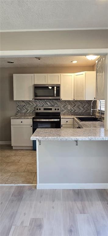 kitchen with light wood-type flooring, a sink, tasteful backsplash, stainless steel appliances, and a peninsula