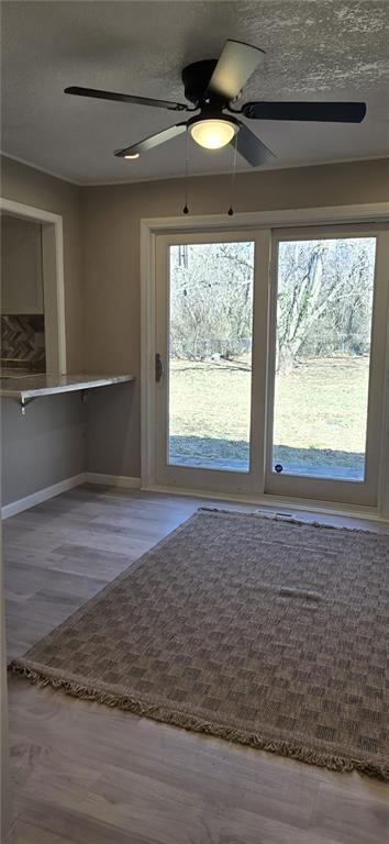 doorway with wood finished floors, a ceiling fan, and baseboards