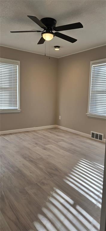 empty room with visible vents, baseboards, ceiling fan, and wood finished floors