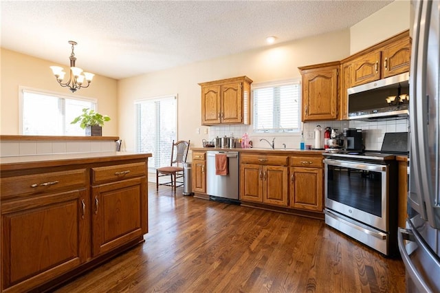 3015 SW 9th Ter, Lees Summit, MO 64081 - kitchen with an inviting chandelier, brown cabinetry, a sink, stainless steel appliances, and backsplash