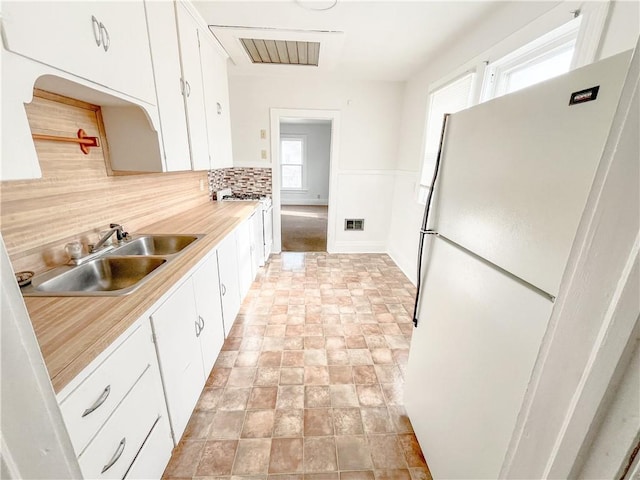 kitchen with freestanding refrigerator, a sink, light countertops, white cabinets, and backsplash