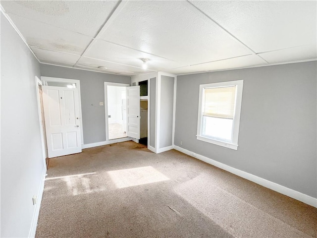 unfurnished bedroom featuring a paneled ceiling, baseboards, and carpet floors