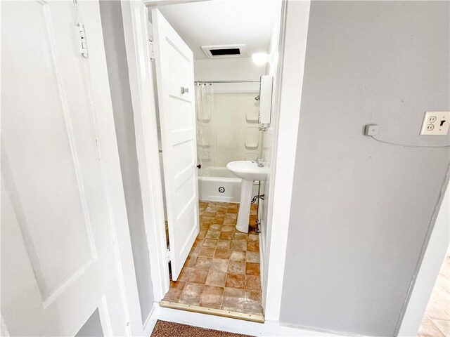 bathroom with stone finish floor, shower / bath combo, visible vents, and a sink
