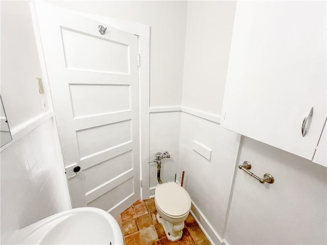 half bath with tile patterned floors, a wainscoted wall, toilet, and tile walls