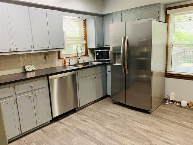 kitchen featuring dark countertops, appliances with stainless steel finishes, a sink, light wood-style floors, and plenty of natural light