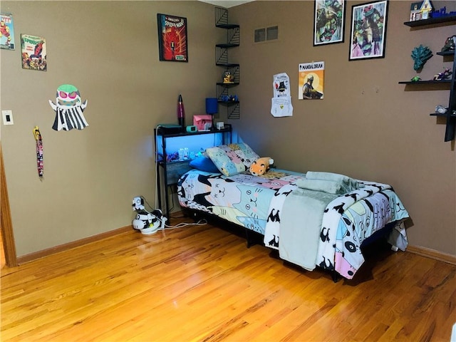 bedroom with baseboards, visible vents, and wood finished floors