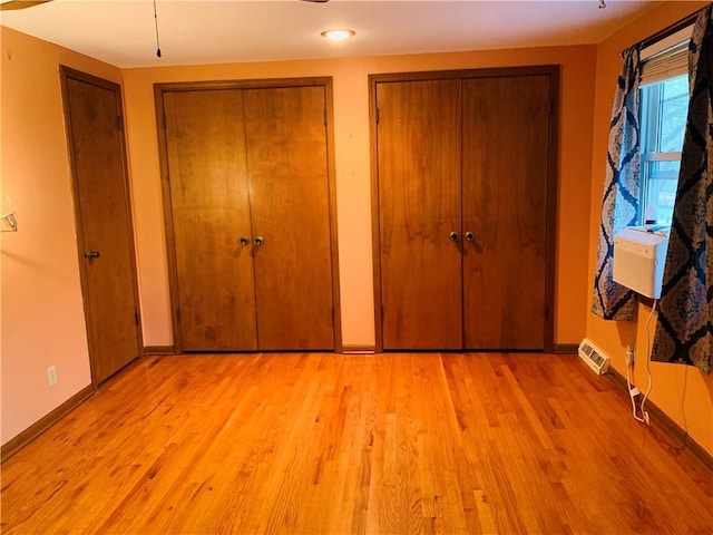 unfurnished bedroom featuring baseboards, multiple closets, and light wood finished floors