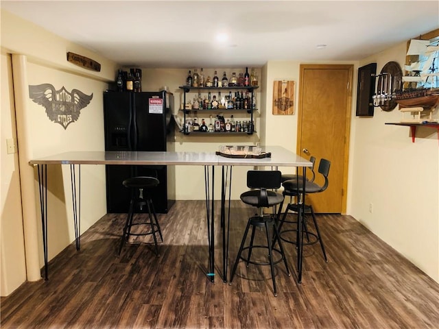 bar featuring a bar, black refrigerator with ice dispenser, and dark wood-type flooring