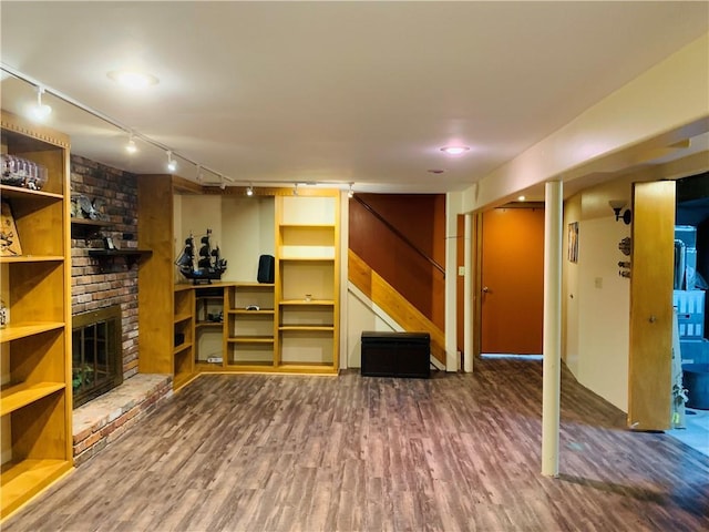 finished below grade area with a brick fireplace, rail lighting, wood finished floors, and stairway