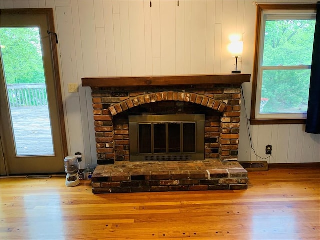 interior details featuring baseboards, a brick fireplace, wood walls, and wood finished floors