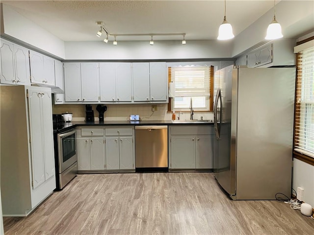 kitchen featuring a sink, light wood-style flooring, dark countertops, and stainless steel appliances