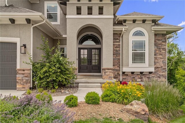 9238 Marion St, Lenexa, KS 66220 - entrance to property featuring french doors, stucco siding, stone siding, an attached garage, and a shingled roof