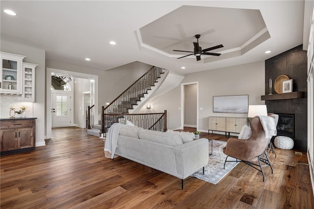 9238 Marion St, Lenexa, KS 66220 - living area with dark wood finished floors, a tray ceiling, recessed lighting, a tiled fireplace, and stairway