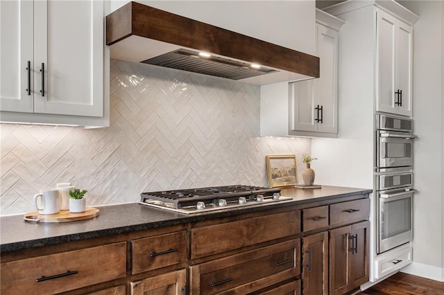 9238 Marion St, Lenexa, KS 66220 - kitchen with stainless steel appliances, custom exhaust hood, dark countertops, decorative backsplash, and white cabinets