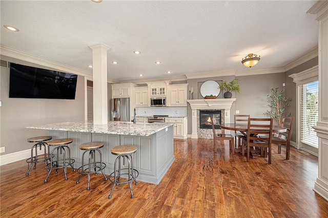 15511 Salem Rd, Excelsior Springs, MO 64024 - kitchen featuring appliances with stainless steel finishes, baseboards, a glass covered fireplace, decorative columns, and ornamental molding