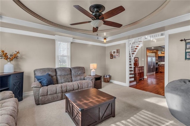 carpeted living room featuring crown molding, baseboards, ceiling fan, stairway, and a tray ceiling