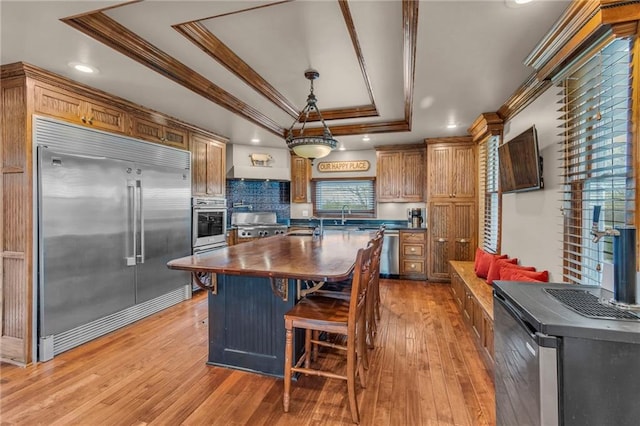 kitchen featuring crown molding, appliances with stainless steel finishes, a sink, light wood-style floors, and a tray ceiling
