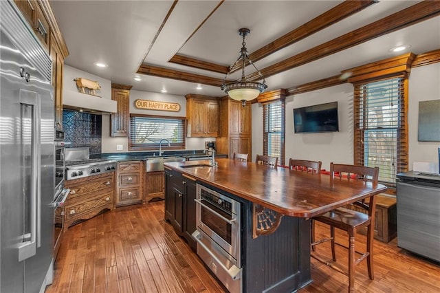 kitchen with a sink, ornamental molding, appliances with stainless steel finishes, and a raised ceiling
