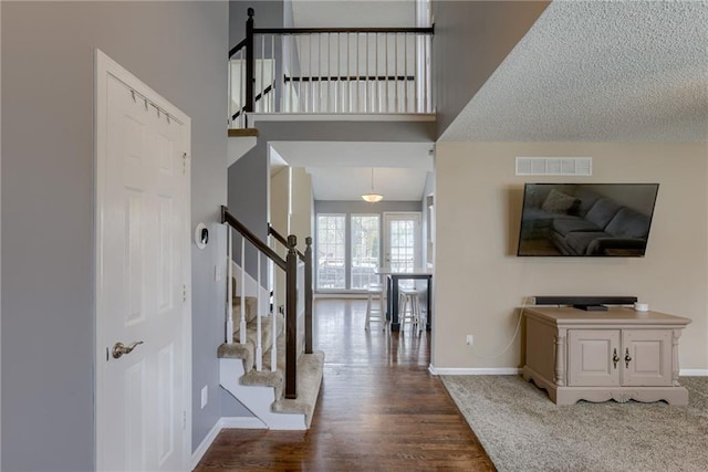 entrance foyer featuring visible vents, baseboards, a high ceiling, stairway, and wood finished floors