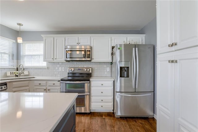 kitchen with hanging light fixtures, a sink, appliances with stainless steel finishes, white cabinetry, and backsplash