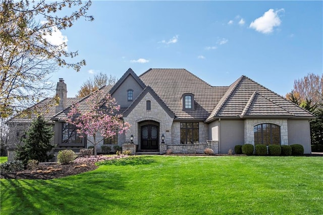 view of front of property featuring a front yard, stone siding, stucco siding, french doors, and a chimney