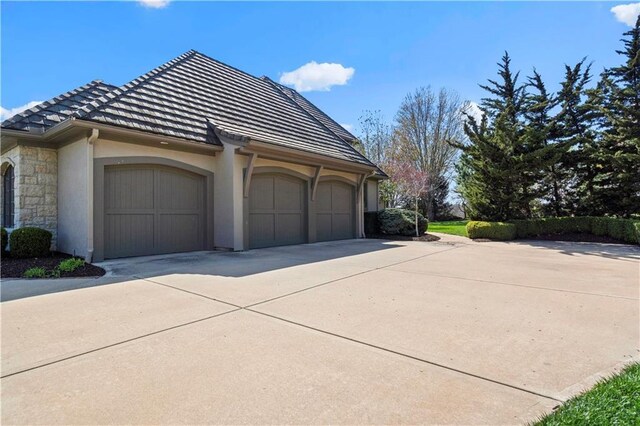 10408 Howe Ln, Leawood, KS 66206 - view of property exterior featuring a garage, stone siding, stucco siding, concrete driveway, and a tile roof