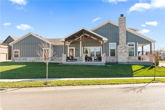 back of property with a lawn, board and batten siding, stone siding, and a chimney