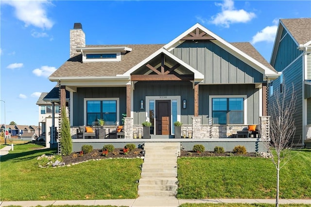 view of front of home with board and batten siding, covered porch, a front yard, a shingled roof, and a chimney