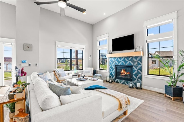 living area with a ceiling fan, baseboards, light wood finished floors, a fireplace, and a towering ceiling