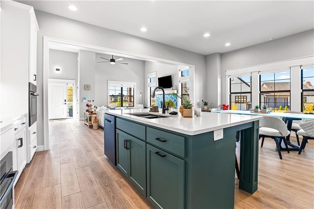 kitchen featuring green cabinetry, light wood-style flooring, a sink, light countertops, and white cabinetry