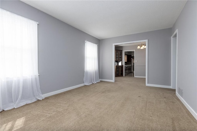 empty room with baseboards, an inviting chandelier, visible vents, and light carpet