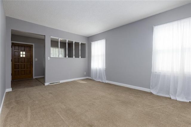 carpeted spare room with baseboards, visible vents, and a textured ceiling