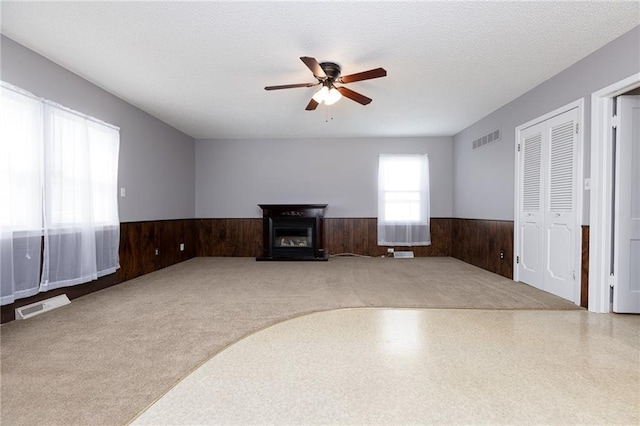 unfurnished living room with wainscoting, wooden walls, visible vents, and ceiling fan