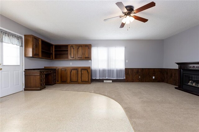 kitchen with a ceiling fan, open shelves, a textured ceiling, wainscoting, and brown cabinetry