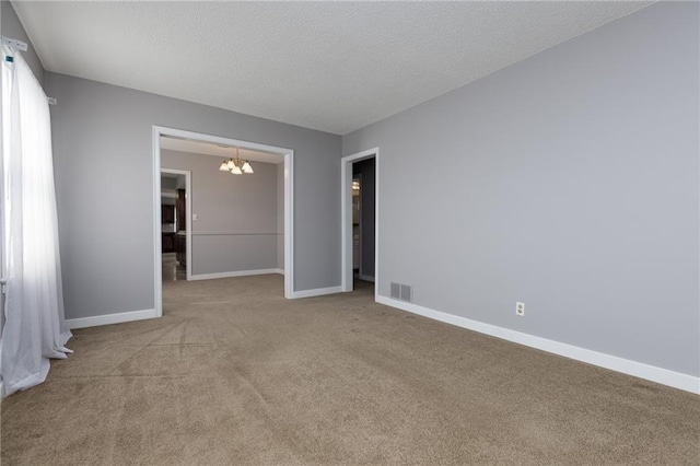 carpeted empty room with baseboards, visible vents, a textured ceiling, and a chandelier