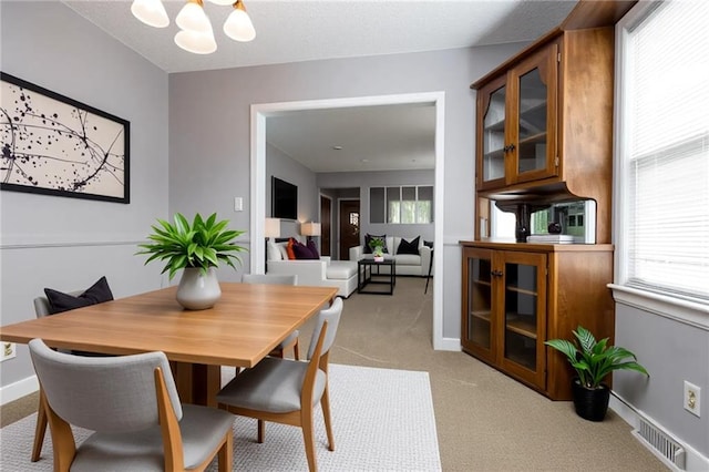 dining room featuring a chandelier, visible vents, baseboards, and light carpet