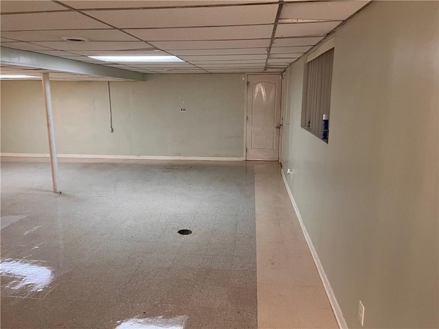 finished basement with tile patterned floors, baseboards, and a paneled ceiling