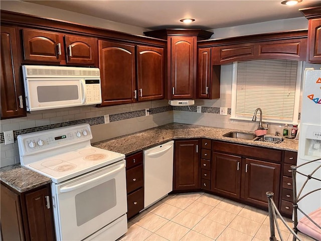 kitchen with a sink, dark stone counters, white appliances, and tasteful backsplash