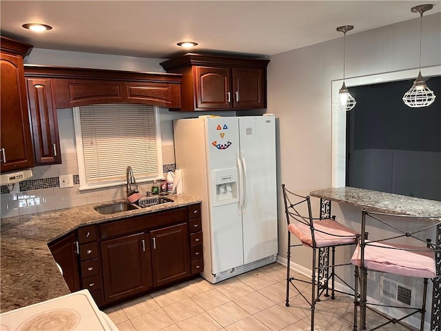 kitchen featuring visible vents, backsplash, decorative light fixtures, white fridge with ice dispenser, and a sink